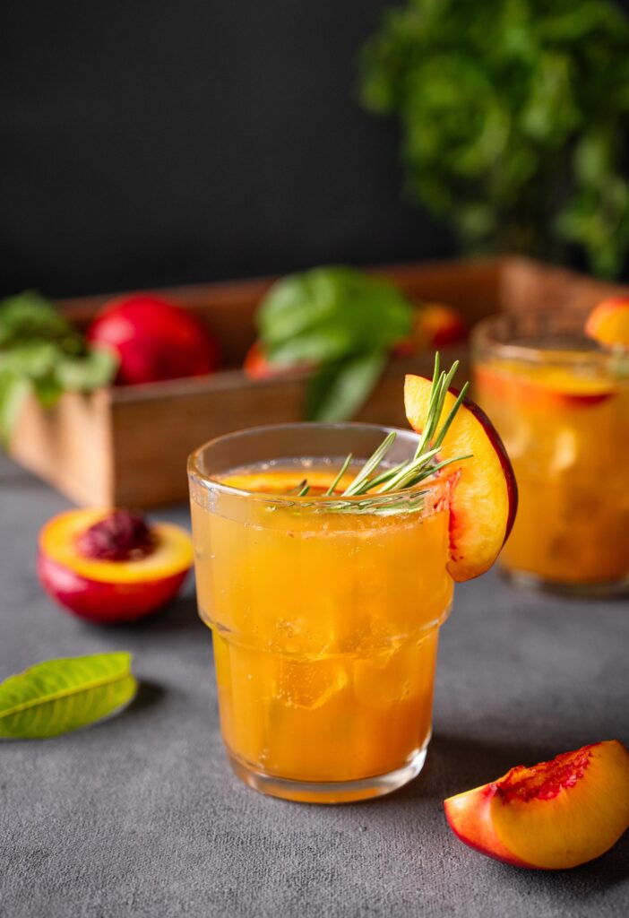 Peach tea with ice and rosemary on a glass. Vegan homemade healthy drink on a dark background
